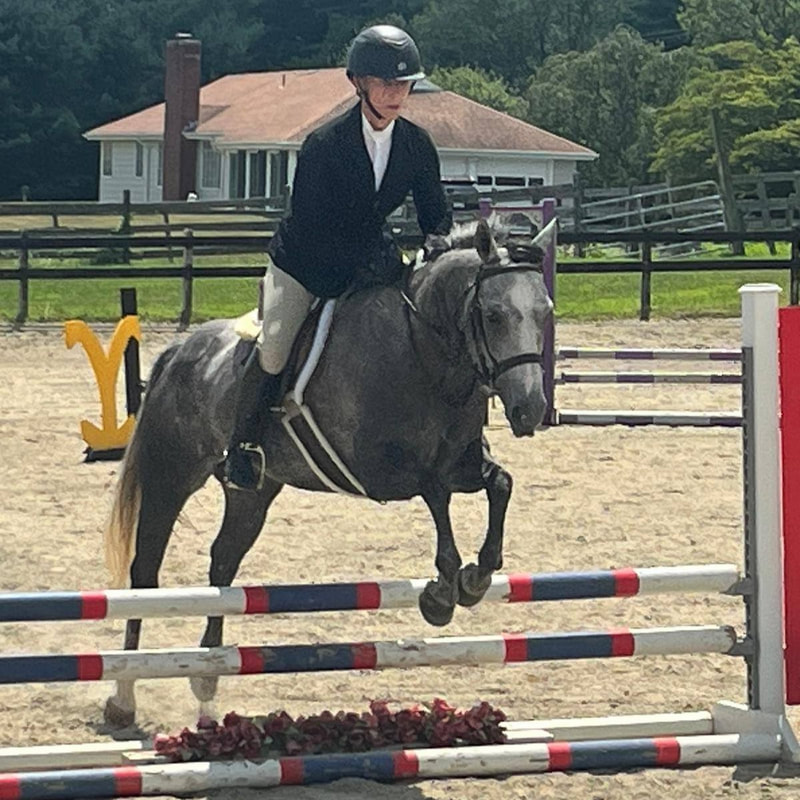 gray pony and rider jumping a fence at a horse show